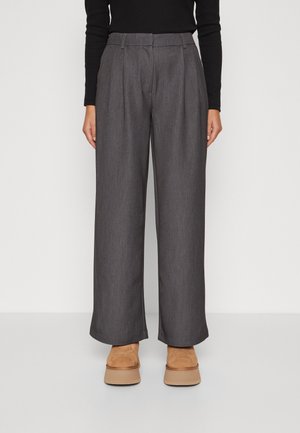 Pantaloni grigi a gamba larga con una finitura testurizzata. Presentano una vita alta, pieghe e tasche frontali angolate. Abbinati a scarpe con zeppa color marrone.