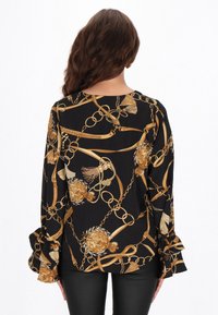 Fekete blúz arany lánccal és virágmintákkal. Hosszú ujjakkal, fodros mandzsettákkal. Puha anyagból, kényelmes szabással.