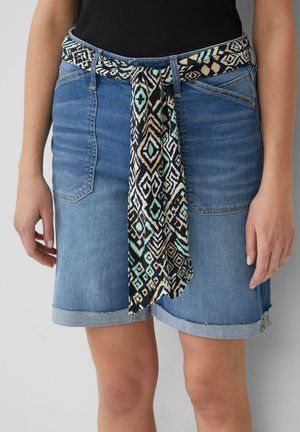Jupe en denim avec une ceinture en tissu à motifs présentant des designs géométriques en noir, vert canard et beige. La jupe a un ourlet effiloché et des poches latérales.