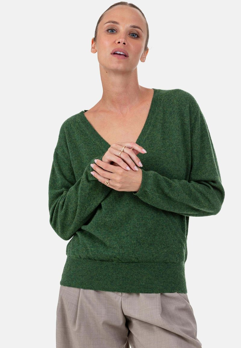 Grüner Strickpullover mit V-Ausschnitt, weiter Passform und geripptem Saum. Verfügt über lange Ärmel und eine weiche Textur, getragen über hellgrauer Hose.