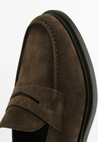 Brune ruskinds loafers med et syet design og en bred stropdetalje. Har en glat sort gummisål og rund tåform.