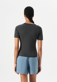 Short-sleeve, dark gray fitted t-shirt with a round neckline. It has smooth, stretchy fabric and raglan sleeves, paired with denim shorts.