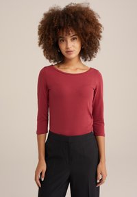 Röd långärmad topp med rund halsringning, gjord av stretchigt material, ihop med högmidjade svarta byxor. Slät textur, kroppsnära passform.