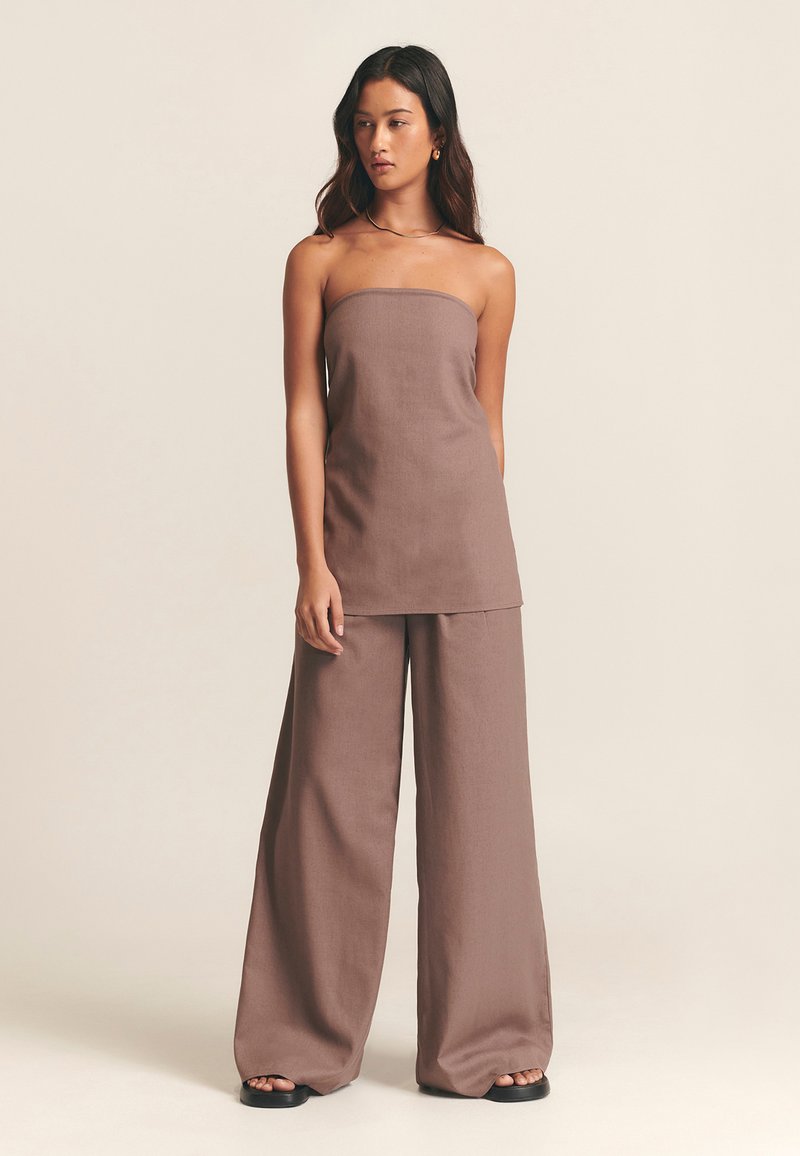 Hnědý top bez ramínek a široké kalhoty z lehké látky. Hladká textura s volným střihem. Minimalistický design bez viditelných vzorů či akcentů.