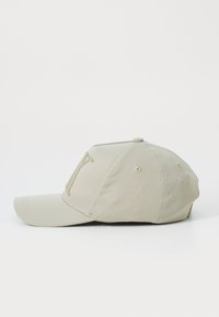 Beige cap with a curved brim, made of smooth fabric. Features a large, embossed logo on the front and ventilation holes on the sides.