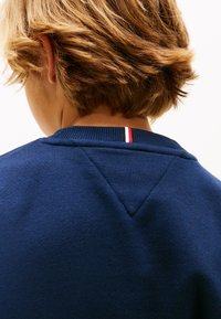 Μπλε φούτερ ναυτικού με ριμπ λαιμόκοψη και τριγωνική λεπτομέρεια στους ώμους. Διαθέτει κόκκινη και λευκή ριγέ λεπτομέρεια στο πίσω μέρος της λαιμόκοψης.