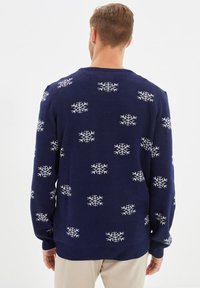 Pull bleu marine avec un motif flocon de neige blanc, texture tricotée, col rond et poignets côtelés. Le design est à la fois décontracté et festif.