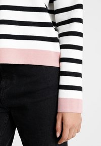 Czarnobiały sweter w paski z różowym dolnym brzegiem. Wykonany z teksturowanej tkaniny o dopasowanym kroju, przedstawiony na czarnym tle z denimu.