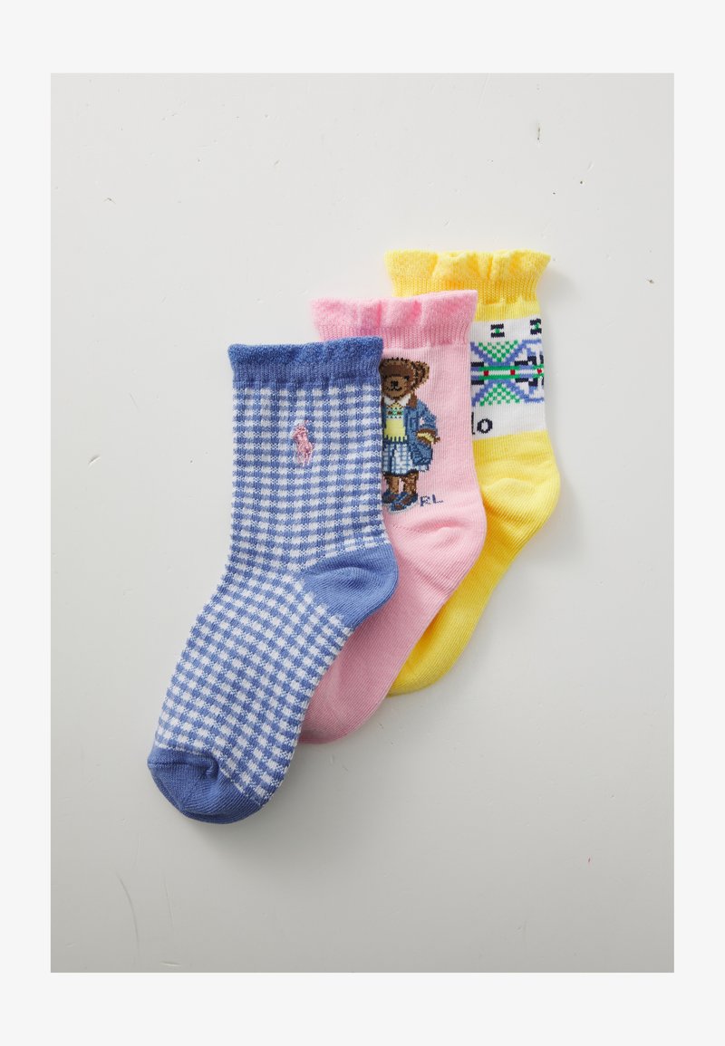 Három pár színes zokni: kék-fehér kockás, rózsaszín medvével díszített, és sárga geometriai mintákkal. Mindegyiknek bordázott a szegélye.