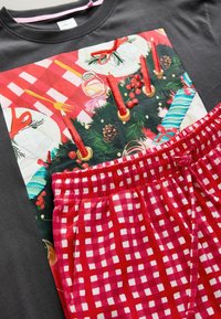 Grauer Sweatshirt mit einem festlichen Druck, der einen dekorierten Tisch und einen Weihnachtskranz zeigt; kombiniert mit rot-weißen karierten Schlafanzughosen.