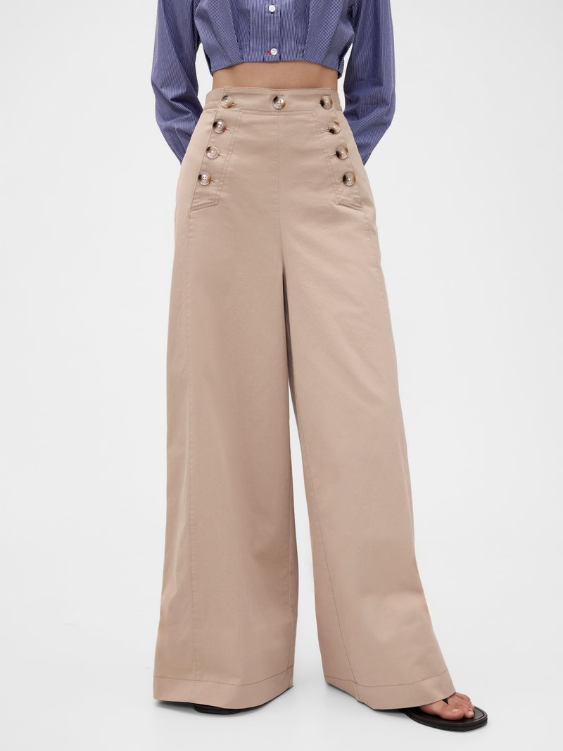 Pantaloni beige a gamba larga con tasche laterali, vita alta e sei bottoni decorativi. Il tessuto sembra liscio con una finitura netta.