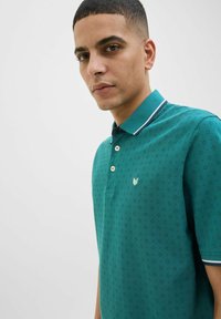 Cămașă polo teal cu un model texturat de mici diamante, guler contrastant cu dungi albe și un mic emblema pe piept.