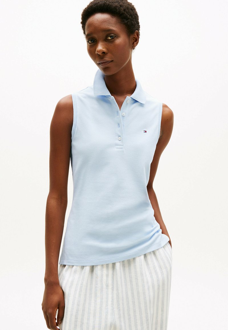 Polo sans manches en coton bleu clair, avec un col et une patte de boutonnage à trois boutons. Petit logo sur la poitrine, associé à un bas rayé.