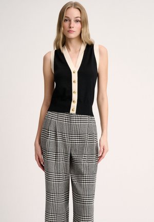 Black sleeveless top with a cream collar and gold buttons, paired with high-waisted, houndstooth patterned trousers in black and white.