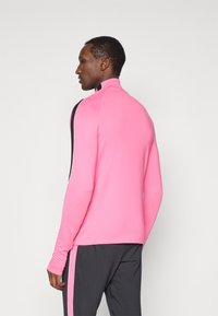 Αθλητική μπλούζα με μακριά μανίκια σε έντονο ροζ χρώμα και υψηλό γιακά, διαθέτει μαύρες και άσπρες πλαϊνές ρίγες και ελαστικό ύφασμα για άνεση.