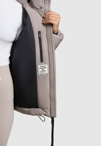 Giubbotto imbottito con un rivestimento esterno grigio, fodera interna nera, tasca con zip e etichetta in tessuto con la scritta "Un caldo abbraccio fatto di stoffa."