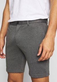 Pantaloni shorts grigi realizzati in tessuto testurizzato, dotati di chiusura a bottone, design aderente e vita liscia. I pantaloni shorts si fermano sopra il ginocchio.