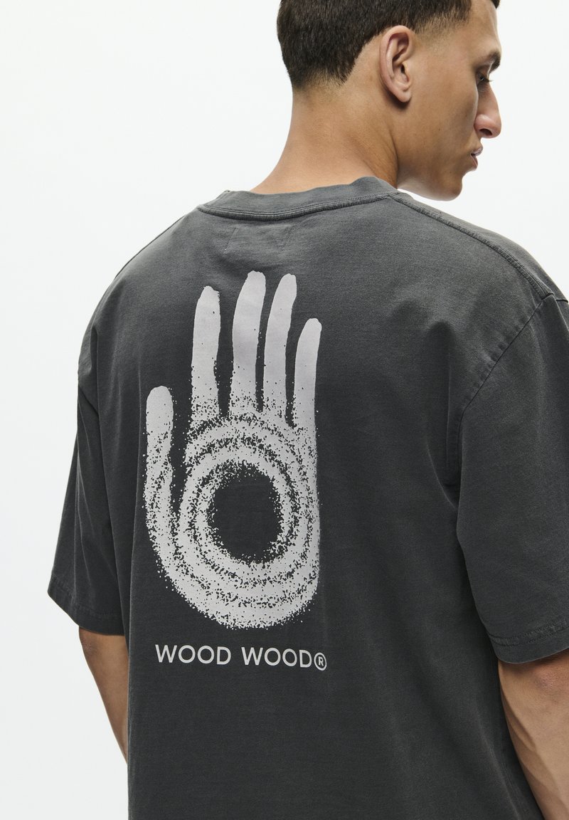 T-shirt en coton gris présentant un grand motif de main blanche avec un design circulaire et le texte "WOOD WOOD" en bas au dos.