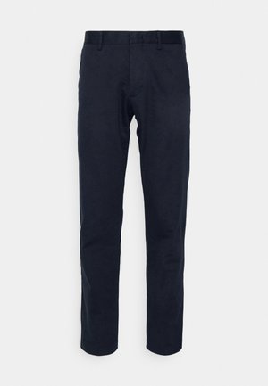 Laivastonsiniset suoralahkeiset housut, joissa on vyönlenkit, etuvetoketju ja hillittyjä yksityiskohtia, esillä yksiväristä taustaa vasten.