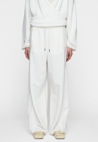 Pantaloni bianchi a gamba larga realizzati in tessuto morbido con vita elasticizzata e coulisse, dotati di due tasche laterali e una sottile texture.
