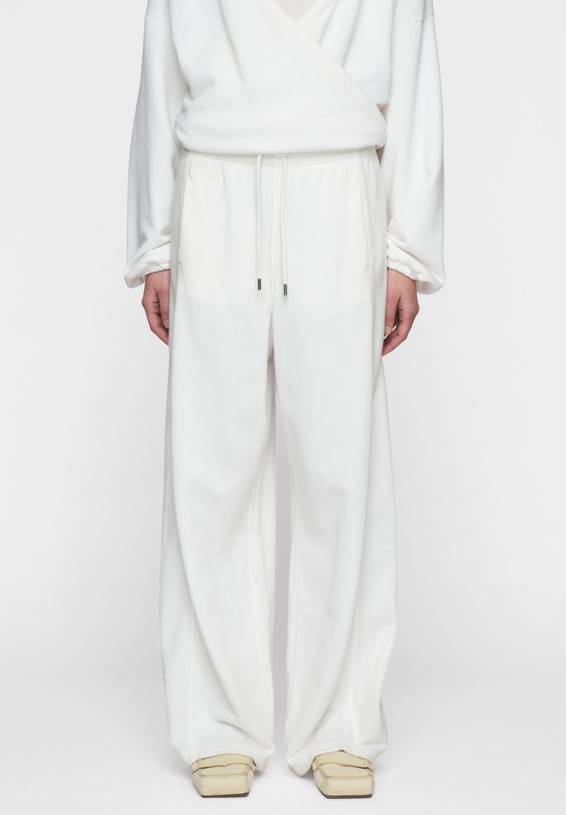 Pantaloni bianchi a gamba larga realizzati in tessuto morbido con vita elasticizzata e coulisse, dotati di due tasche laterali e una sottile texture.