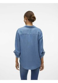 Camicia di denim azzurra chiara, con colletto, maniche lunghe con risvolti e orlo curvo. Tessuto morbido con una consistenza liscia.