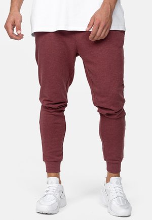 Burgunder joggebukser i blødt, struktureret stof med tapered ankel, båret med hvide sportsko, der har en afslappet pasform, der er velegnet til aktivt tøj.