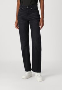 Vaqueros de mezclilla negra con un diseño de pierna recta, cintura alta y estilo de cinco bolsillos. La tela tiene una textura suave; combinados con zapatillas blancas.