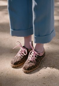 Scarpe stringate con stampa leopardata e lacci rosa, abbinate a calzini rosa chiaro e pantaloni blu cropped.