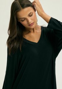 Czarna, luźna bluzka z dekoltem w serek i długimi rękawami, wykonana z gładkiego materiału. Charakteryzuje się minimalnym zdobieniem oraz swobodnym krojem.