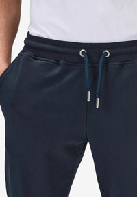 Tummansiniset collegehousut, jotka on valmistettu pehmeästä materiaalista. Niissä on naru vyötäröllä, jossa on hopeanväriset päätypäät, ja sivutaskut kätevyyden vuoksi.