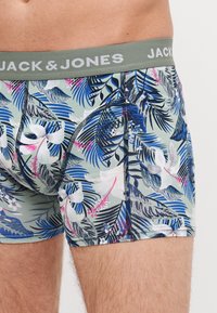 Heren boxershorts van lichtgroene stof met meerkleurige tropische bladeren en bloempatronen, voorzien van een grijze elastische tailleband met de inscriptie "JACK & JONES."