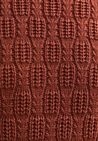 Garen textiel in roestkleur met een textuurpatroon van verweven ovalen en opengewerkte secties, die een rijke, tastbare oppervlakte laat zien.