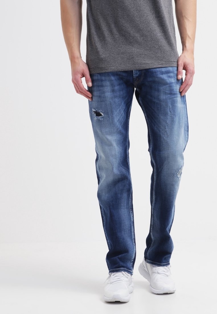 Jeans i medelblå nyans med lätt slitningar och lappar. Rakt skuren design, matchad med en grå t-shirt och vita sneakers.
