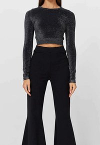 Top corto nero scintillante con maniche lunghe, design aderente e scollatura rotonda. Abbinato a pantaloni neri a palazzo con vita alta.