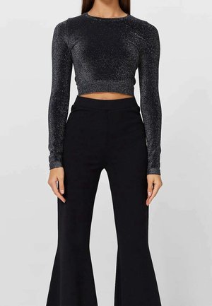 Funkelndes schwarzes Crop-Top mit langen Ärmeln, taillierter Passform und rundem Ausschnitt. Kombiniert mit schwarzen, weit geschnittenen, hoch taillierten Hosen.