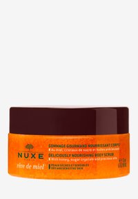 Orange burk med ett mörkbrunt lock, märkt "Nuxe Rêve de Miel" kroppsskrubb. Nyckelingredienser inkluderar honung och sockerkristaller. Kapacitet på 175 ml.