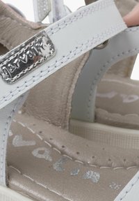 Las sandalias de cuero blanco cuentan con un emblema en tono plateado, correas ajustables y una plantilla suave en beige con detalles perforados.