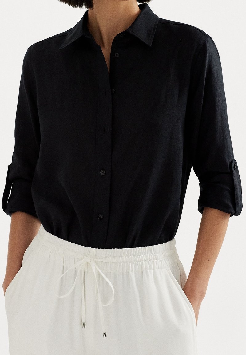 Black button-up shirt made of lightweight fabric with rolled sleeves, paired with white elastic waist pants featuring drawstrings.