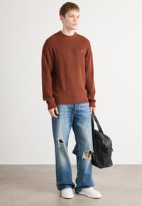 Bruine geribbelde gebreide trui, lichtblauwe distressed jeans met scheuren, witte sneakers en een zwarte leren tas. Eenvoudige, casual outfit.