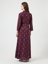 Maxikleid in Kastanienbraun mit blauen Polka-Dots, langen Ärmeln und Kragen. Der Stoff wirkt glatt und hat eine fließende Silhouette.