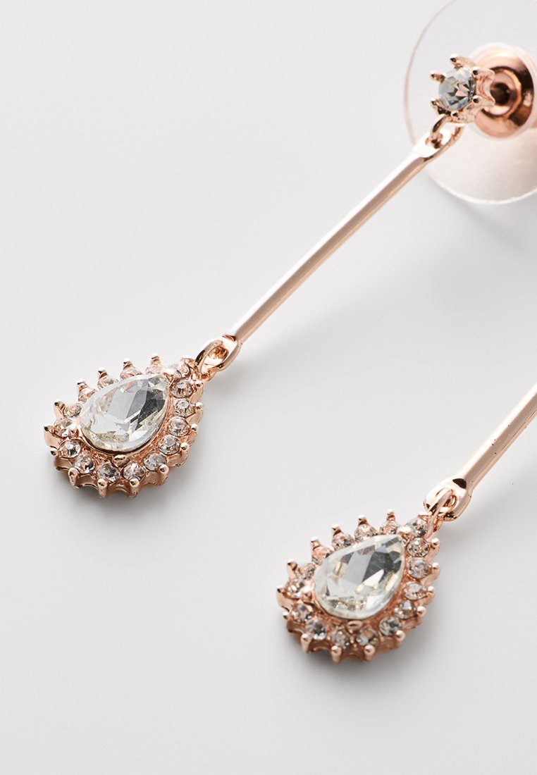 Orecchini a pendente in oro rosa con una pietra chiara a forma di goccia circondata da piccole pietre chiare, dal design elegante e allungato.