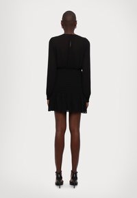 Zwarte jurk met lange mouwen, een gerimpelde taille en een gerimpelde zoom. Gestructureerde stof met doorzichtige details en een kleine opening met sleutelgat aan de achterkant.
