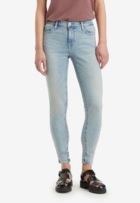 Jeans skinny de color azul claro con un desvanecido sutil, diseño de cinco bolsillos y acentos de costura, combinados con sandalias negras de tiras.
