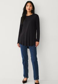 Haut noir à manches longues avec un col rond et un ourlet arrondi, associé à un jean bleu à jambe droite et des ballerines marron pointues.