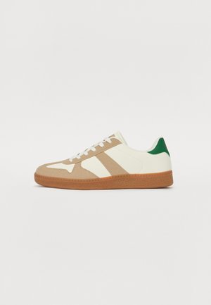 Valged nahast ülemise osaga sneakers, helepruunist seemisnahast pealispinnaga, rohelise kanna aktsendiga ja tekstureeritud kummist tallaga. Omab kolme helepruunist triipu.