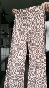 Pantalones de pierna ancha de color marrón y blanco con un diseño de tablero de ajedrez, hechos de una tela suave y flexible con una textura lisa.
