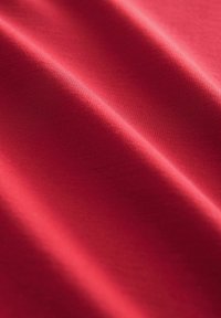 Tissu rouge lisse avec de doux plis et une texture visible en vue rapprochée.
