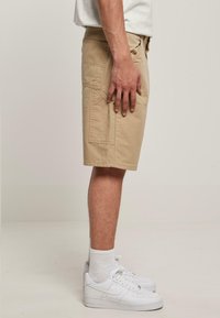 Beige cargo šortky s několika kapsami, vyrobené z odolné tkaniny. Nosené s bílými teniskami Nike a bílými ponožkami do délky lýtek.