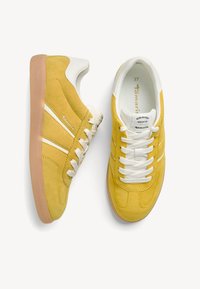 Sneaker gialle in suede con accenti in pelle bianca, chiusura con lacci e suola in gomma marrone chiaro. Presentano dettagli di cucitura e branding.